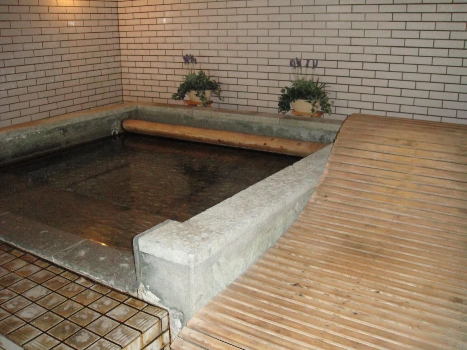 A stone hot spring bath with a wooden edge and tiled floor.