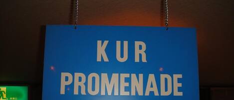 Une pancarte bleue avec du texte blanc indiquant « KUR PROMENADE (健康遶步道) » est suspendue au plafond.