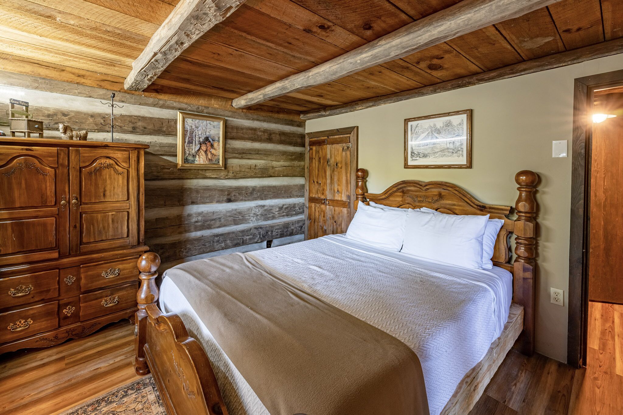 A wooden log cabin bedroom with a large bed, wooden dresser, and two framed pictures on the walls.