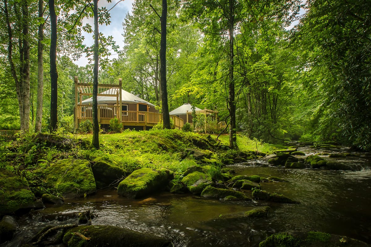 Una cabaña rodeada por un bosque y un arroyo.