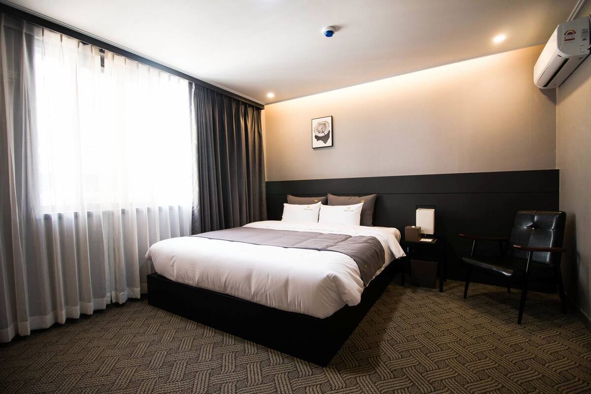 A hotel room with a large bed, a chair, a bedside table, and a picture on the wall.
