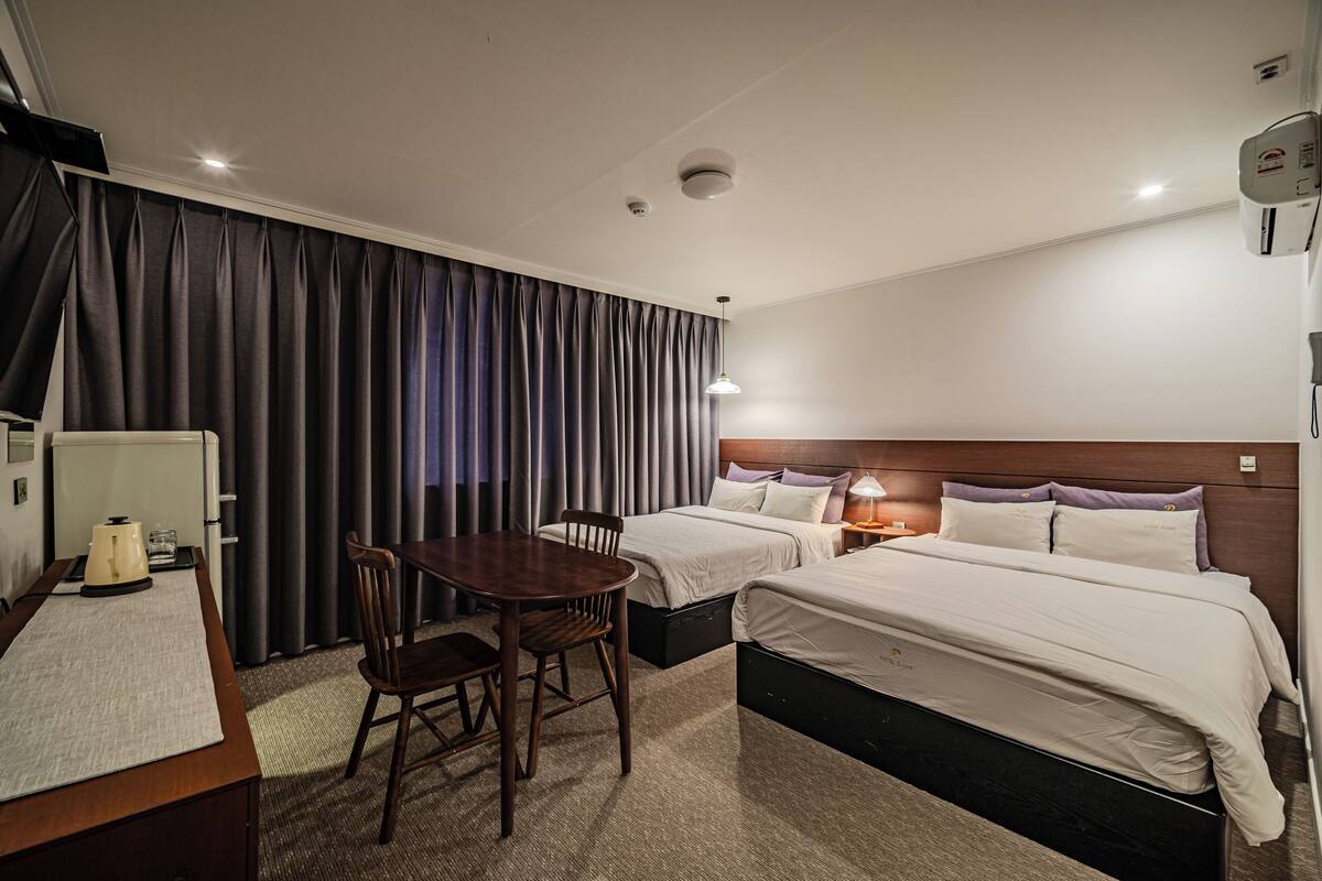 A hotel room with two beds, a desk, a chair, and a table.