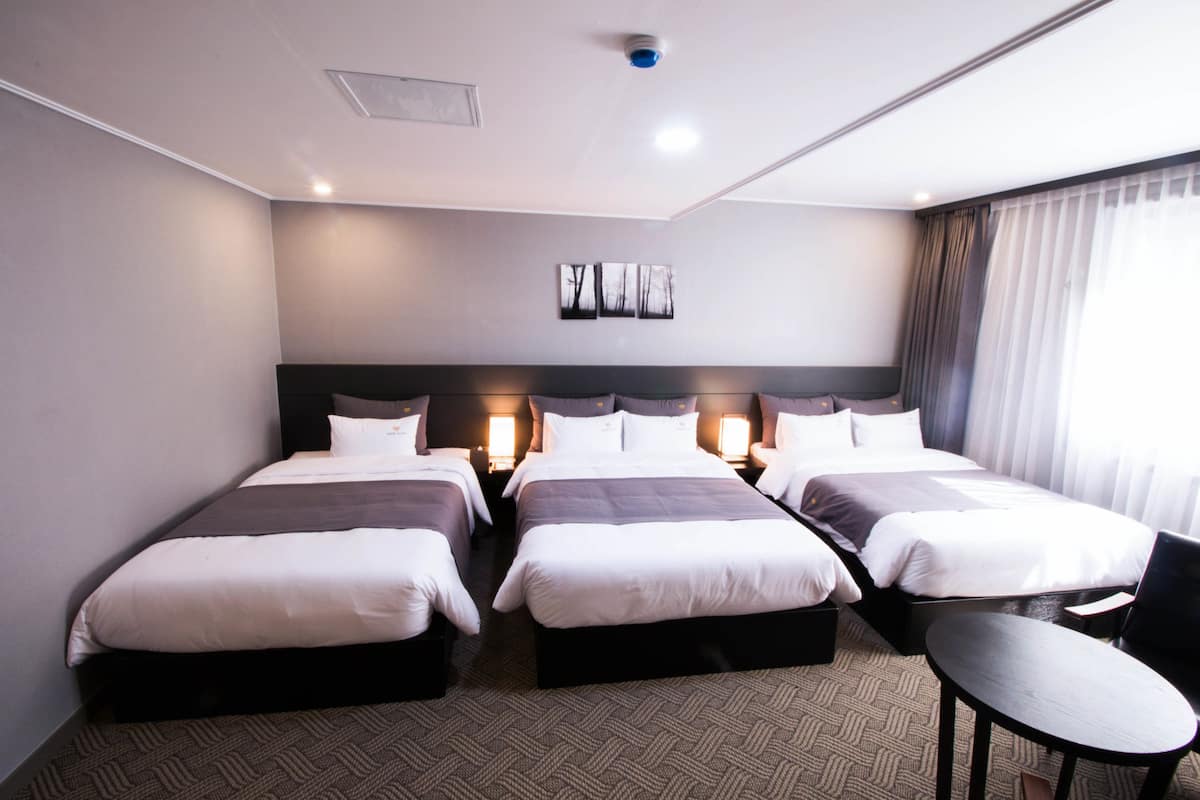 A hotel room with two beds, a small table, and a chair.