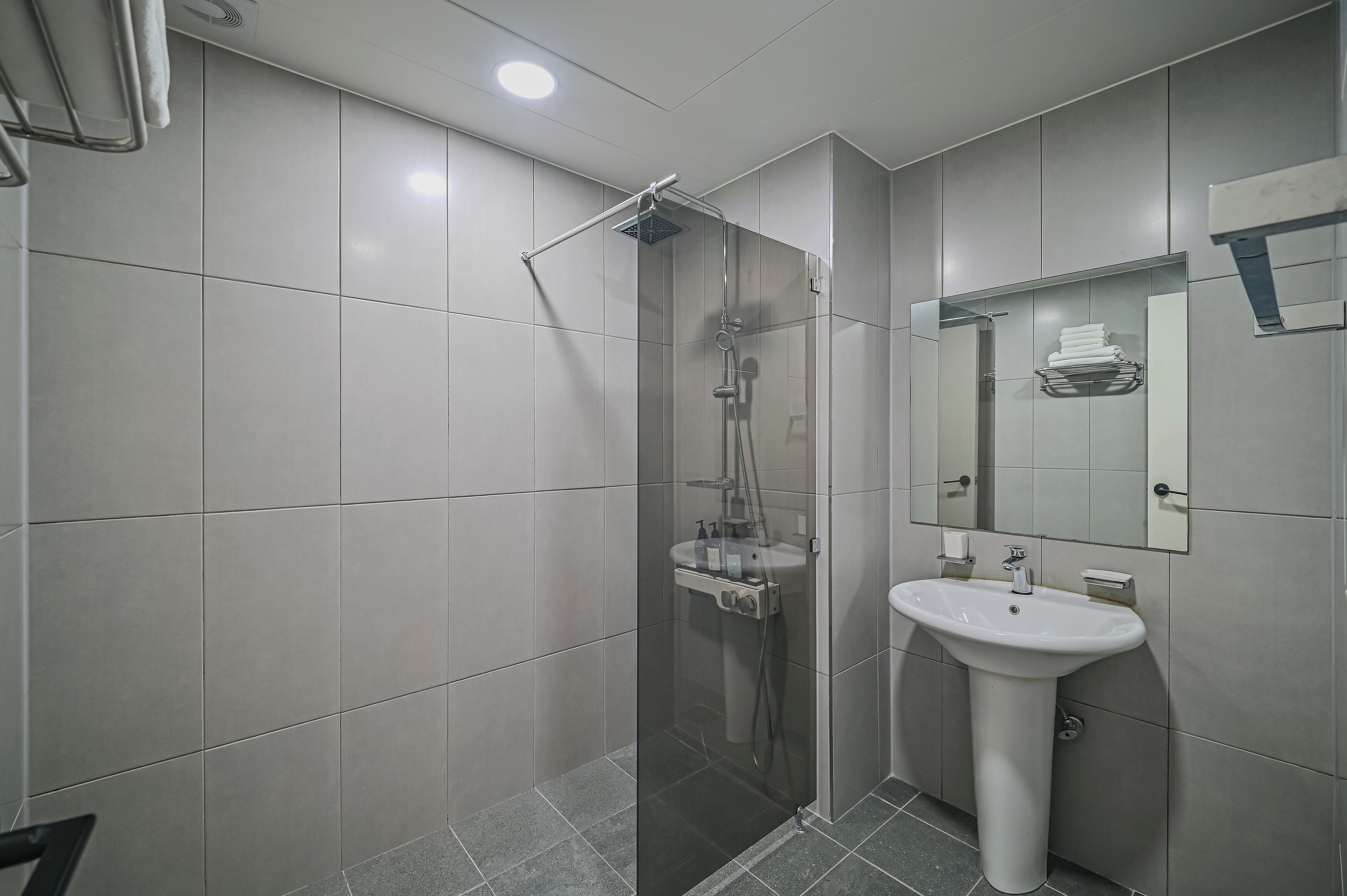 A modern bathroom with a glass-enclosed shower, a pedestal sink, and a mirror with a towel rack.