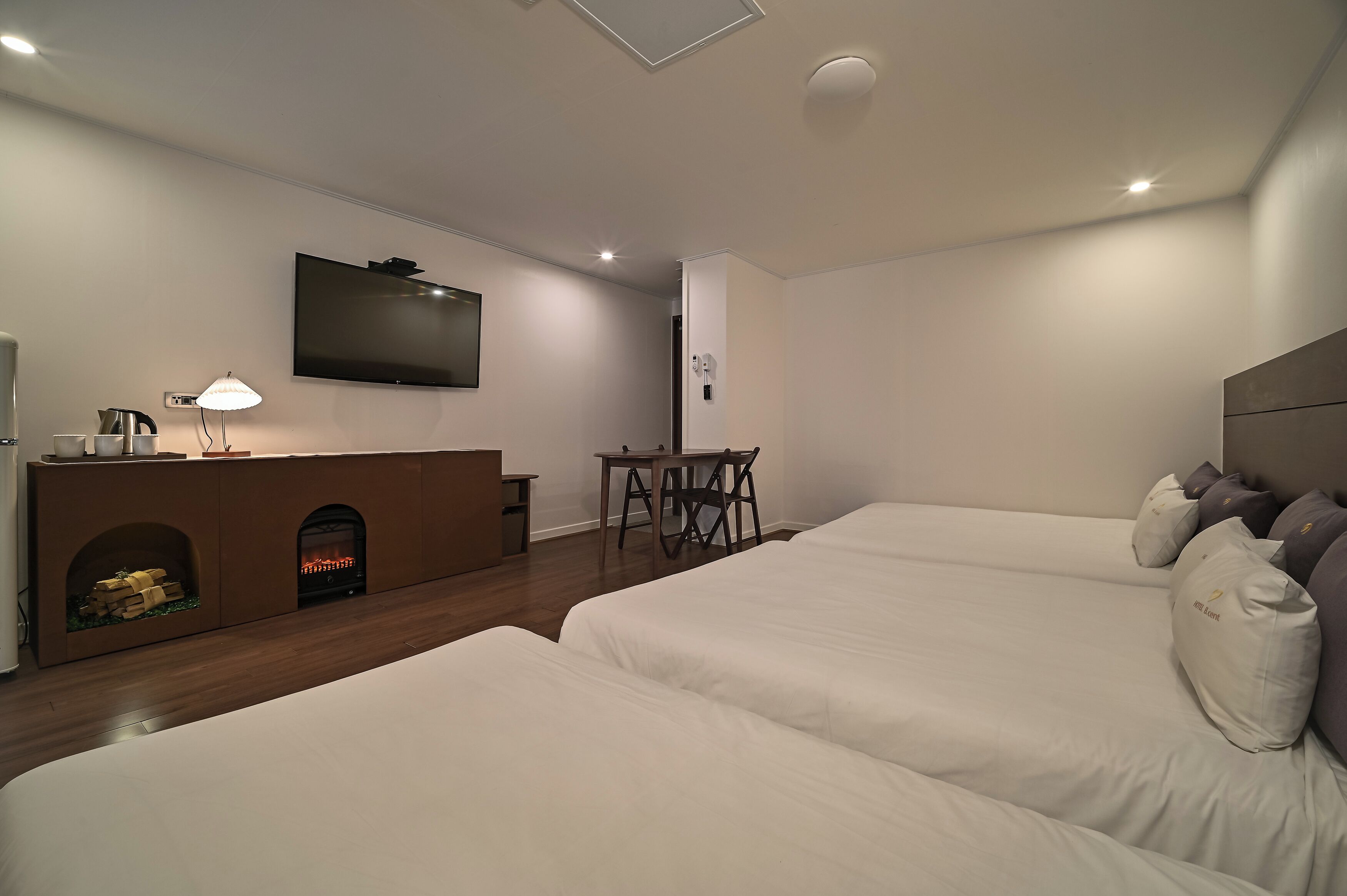 Habitación de hotel moderna con dos camas, una televisión de pantalla plana, chimenea, escritorio y lámpara.