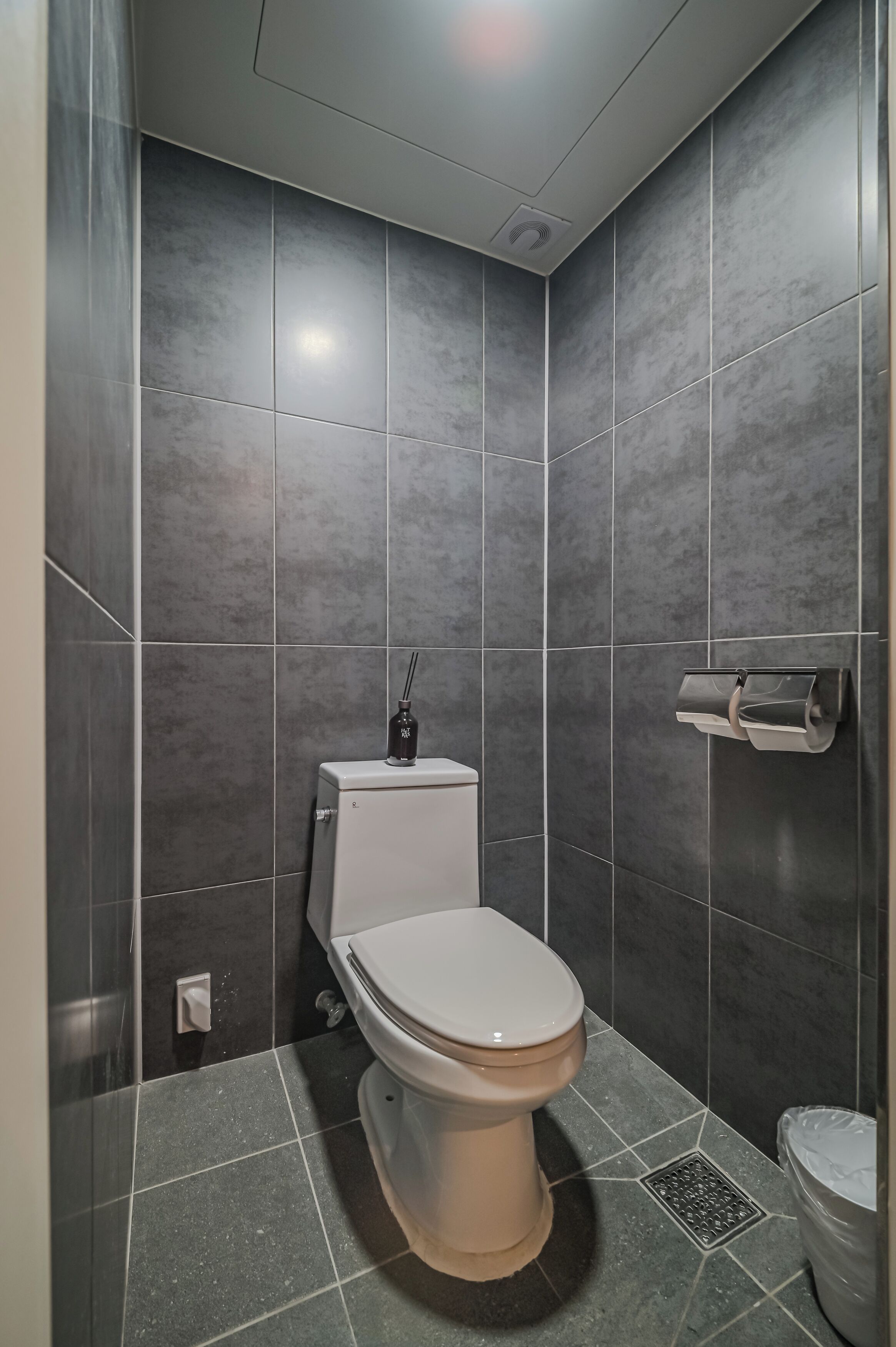 A bathroom with a toilet, a hand dryer, and a trash bin.