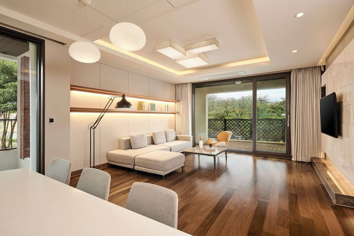 Een moderne woonkamer met een bank, salontafel en stoelen, een trap en een grote glazen schuifdeur die uitkomt op een balkon.
