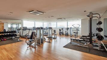 A gym with various exercise equipment, wooden flooring, and large windows.