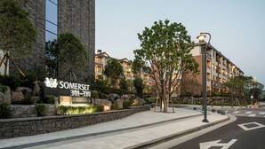 Un edificio moderno con fachada de piedra, un letrero que dice 'Somerset 301-310' y una zona ajardinada con árboles y un sendero pavimentado.