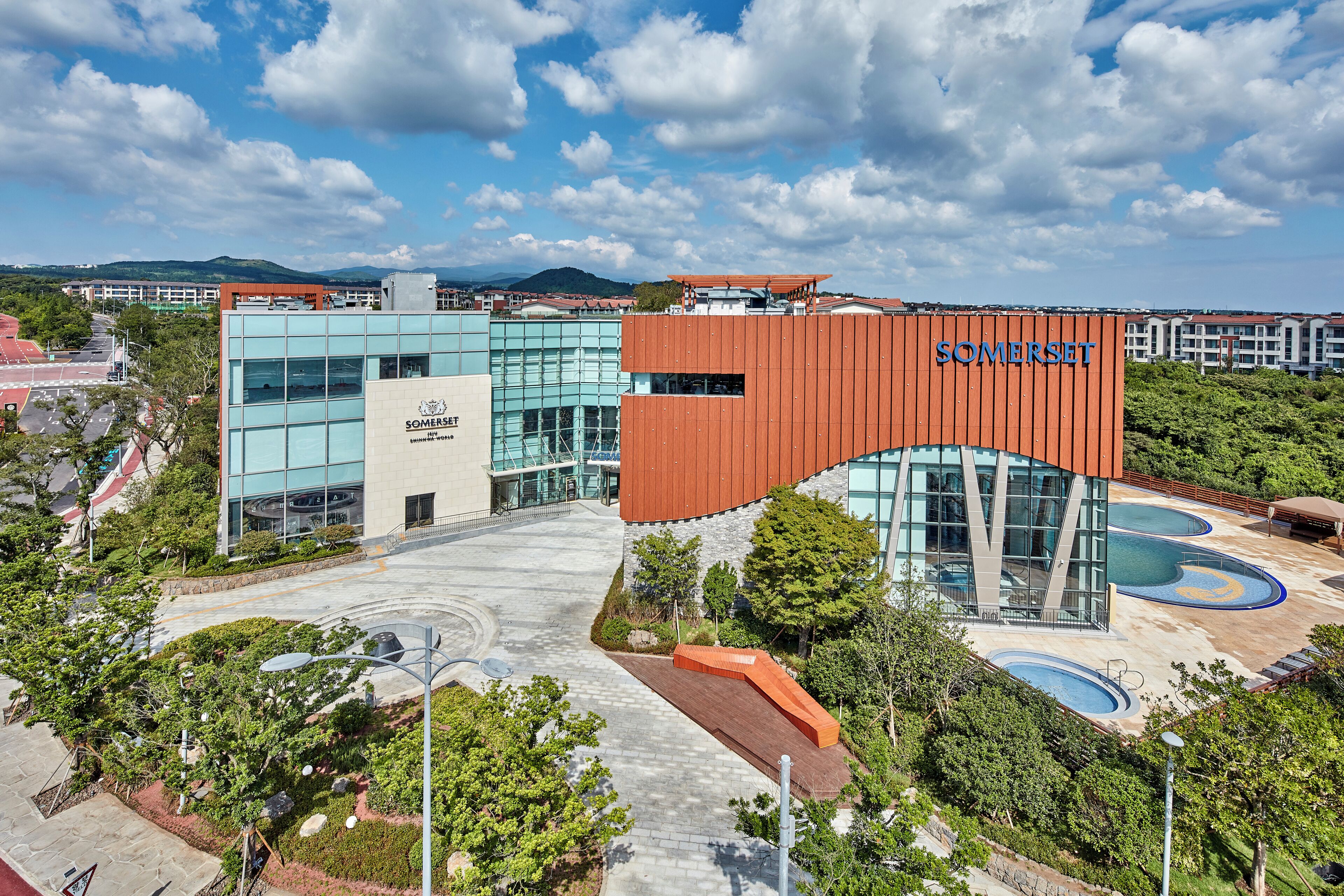 Un edificio moderno con el nombre 'Somerset' bien visible, rodeado de zonas ajardinadas y piscinas.