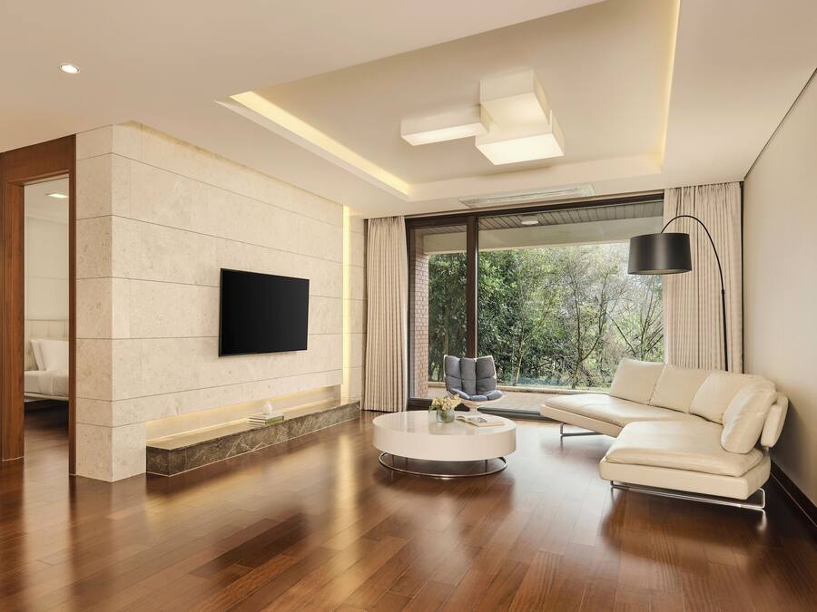 Una sala de estar moderna con un televisor de pantalla plana, un sofá, una mesa de centro y un amplio ventanal con cortinas.