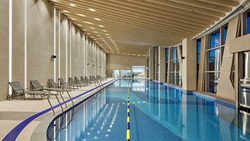 An indoor swimming pool with a long, straight layout, a tiled floor, and a ceiling with evenly spaced lights.