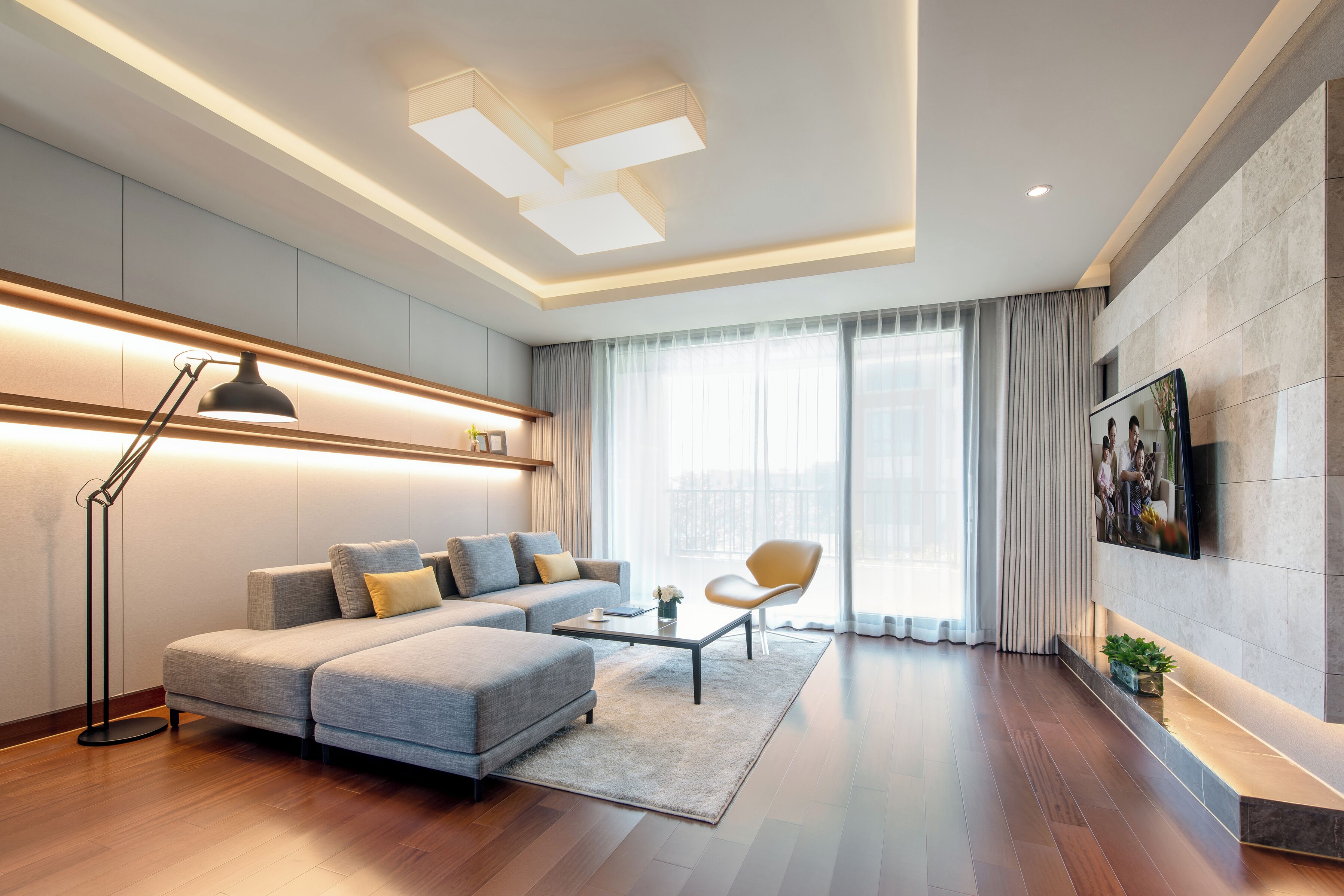 A modern living room with a sectional sofa, a coffee table, a floor lamp, and a TV mounted on the wall.