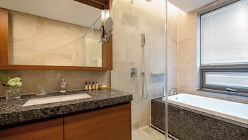 A modern bathroom with a granite countertop, a large mirror, a shower, and a window.