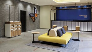 A modern lobby with a reception desk, a yellow sofa, a wooden cabinet, and a patterned ceiling. - Four Points Flex by Sheraton Kanazawa (Kanazawa)