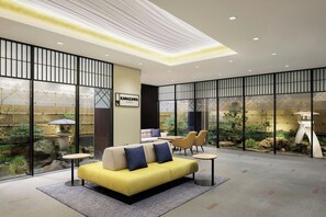Un moderno hall de hotel con un sofá amarillo, zona de estar y vista a un jardín a través de amplios ventanales.