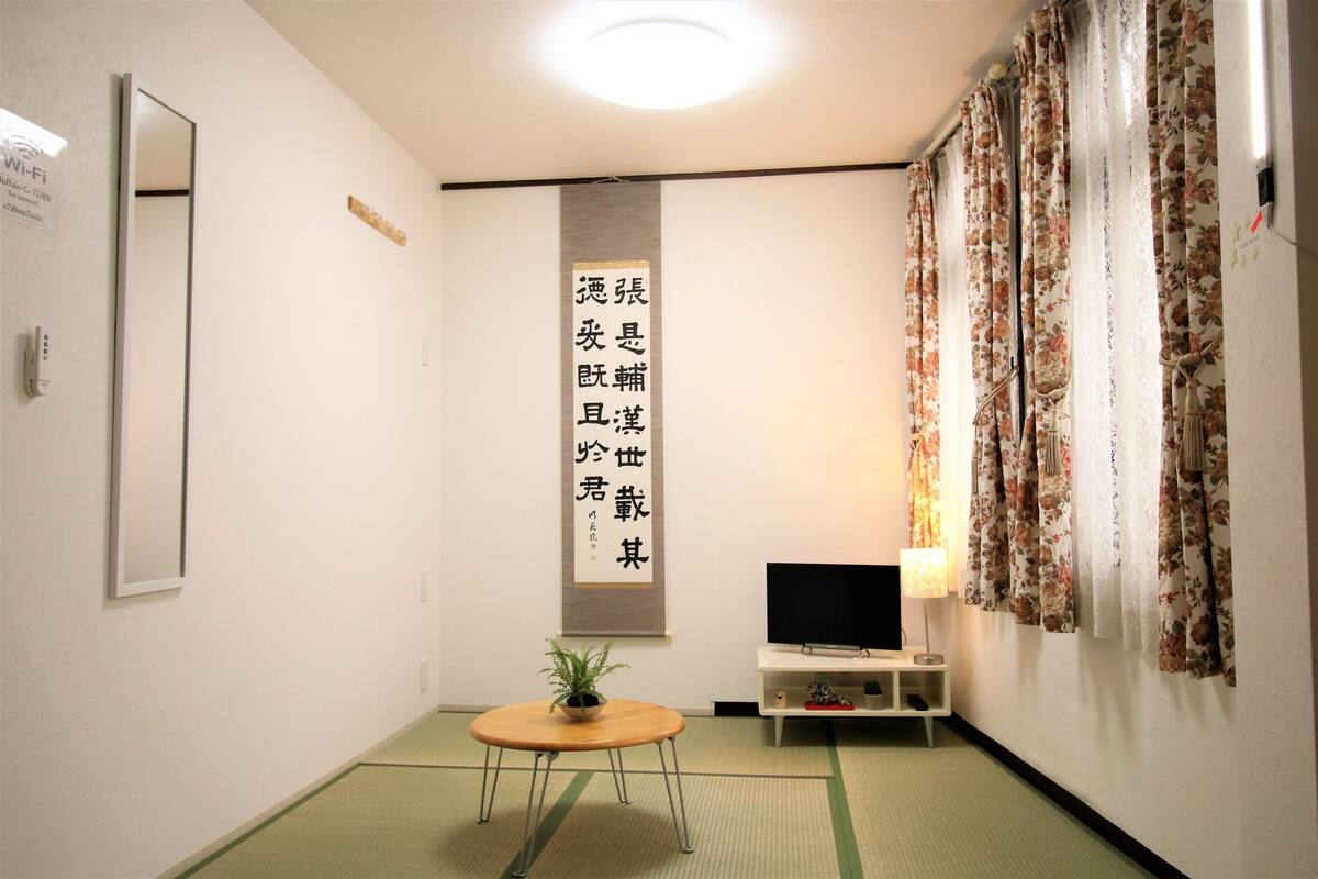 A room with a television, a small table with a plant, and a decorative wall hanging.