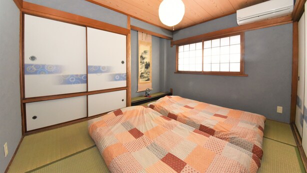 Una habitación japonesa tradicional con suelo de tatami, un futón con manta estampada, puertas correderas y un ventilador de techo.