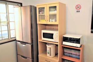 A kitchen with a stainless steel refrigerator, a microwave, a coffee maker, and a shelf with books. - Banana Hammock - Hostel (Osaka)