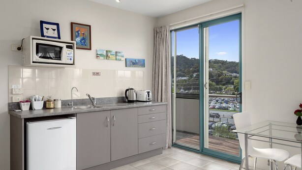 A modern kitchen with a built-in microwave, a small refrigerator, and a dining area with a glass table and chairs.