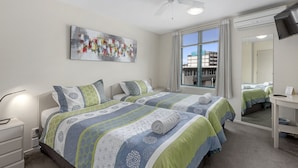 A hotel room with two beds, a ceiling fan, a large window with curtains, a flat-screen TV, and a painting on the wall.