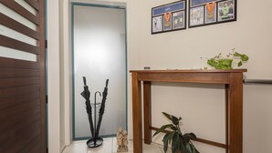 A hallway with a wooden door, a black umbrella stand, a small statue, and a wooden table with a plant.