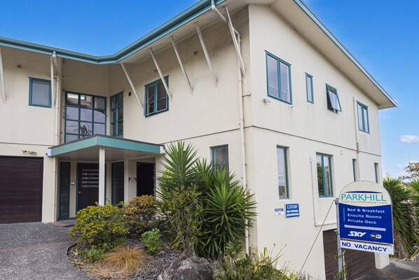 A two-story building with a sign indicating it is a luxury accommodation offering en-suite rooms, breakfast, and a private deck. - Parkhill Fine Accommodation (Whangarei)