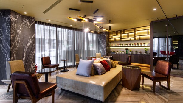 Een moderne hotel lobby met een zithoek, een bar en een groot raam met gordijnen.