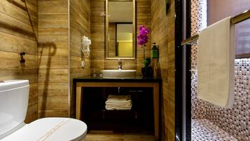 A compact bathroom with wooden walls, a white toilet, a sink with a mirror above it, and a shower area with tiled walls.
