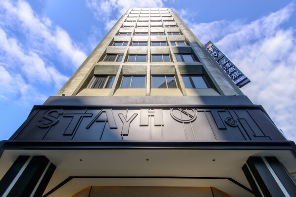 Un immeuble de grande hauteur, surmonté d’une grande enseigne lumineuse indiquant « STAY ».