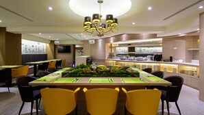 Een moderne eetruimte met een centrale tafel voor vier personen, omringd door gele stoelen, en een keuken in de achtergrond.