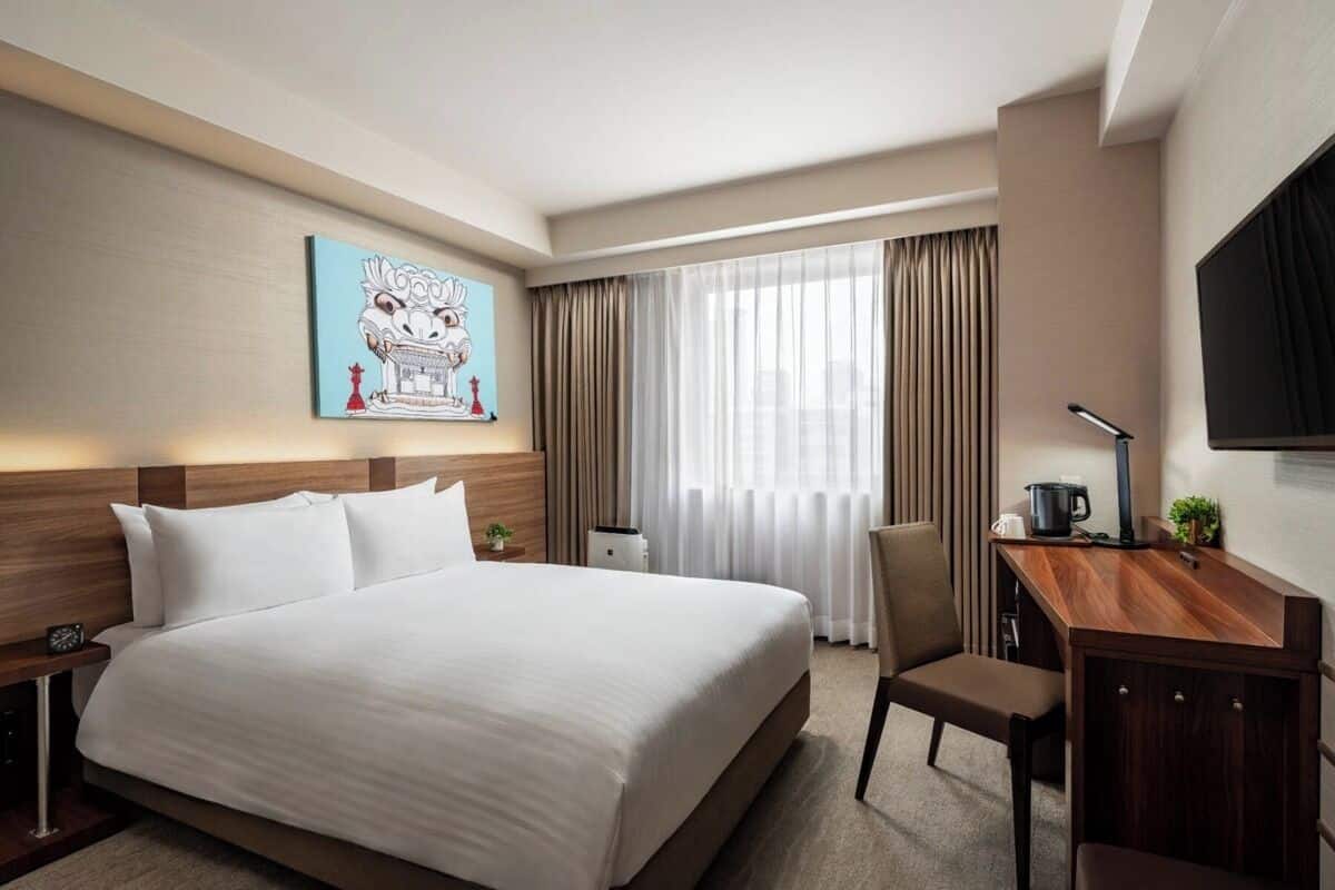 A hotel room with a large bed, a desk, a chair, a television, and a painting on the wall.