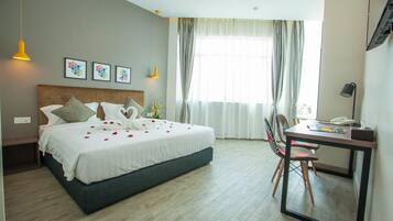 A hotel room with a bed, a desk, and a chair. There are curtains on the window, and a lamp on the desk.