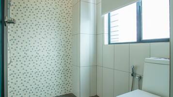 A bathroom with a toilet, shower, and a window.