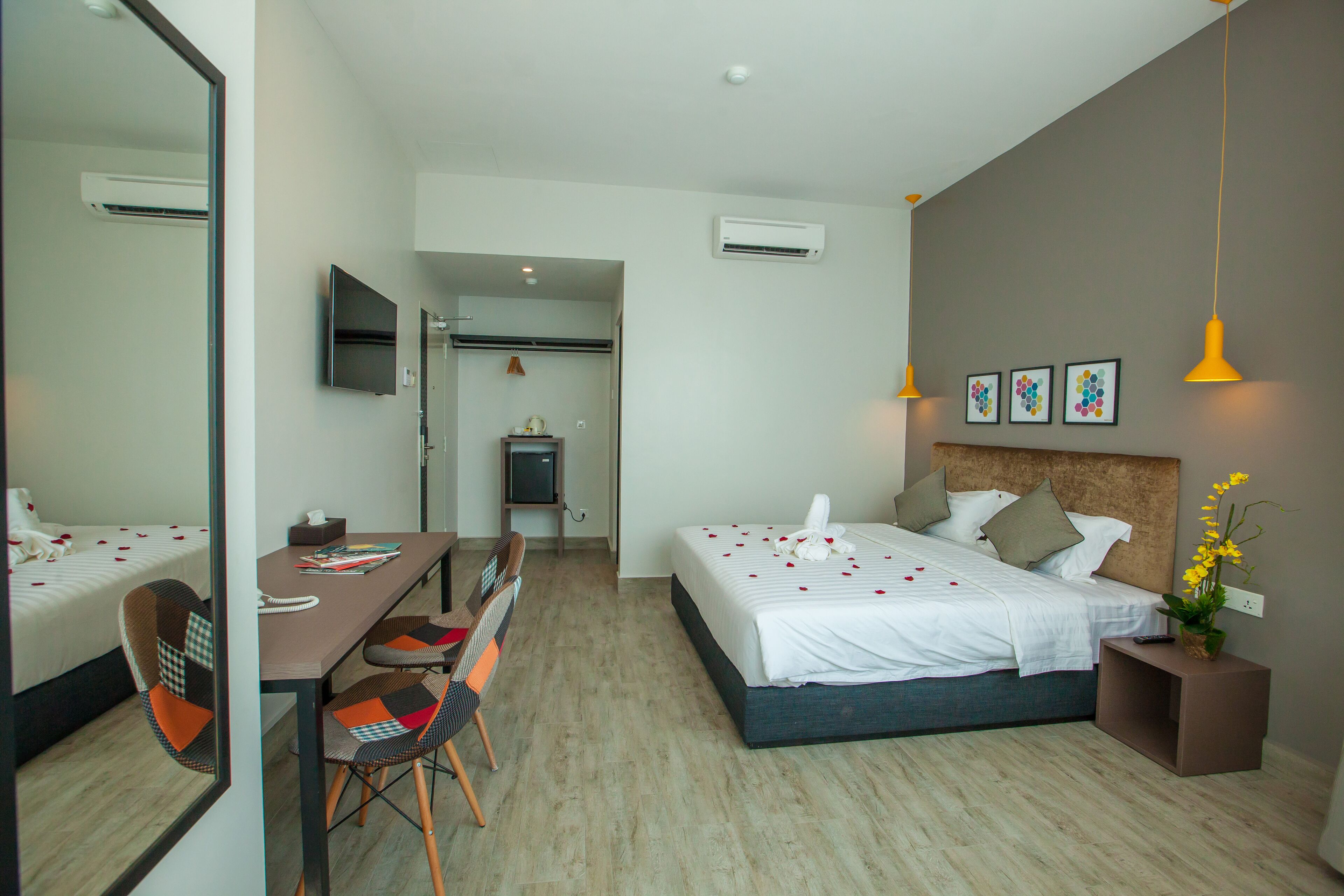 A hotel room with a bed, a desk, chairs, a TV, and a small table with a plant.