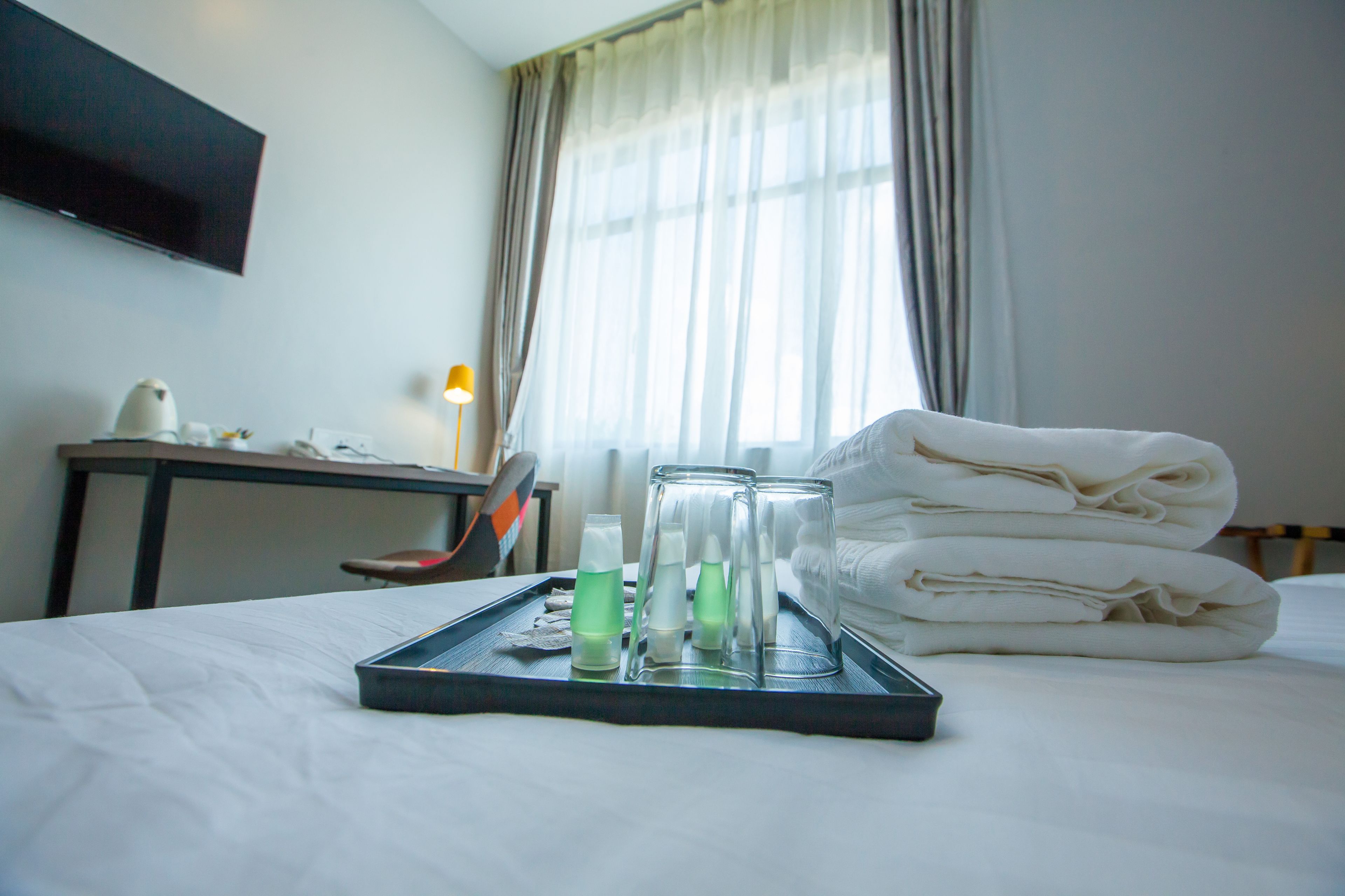 A hotel room with a bed, a tray with toiletries, and a TV on the wall.