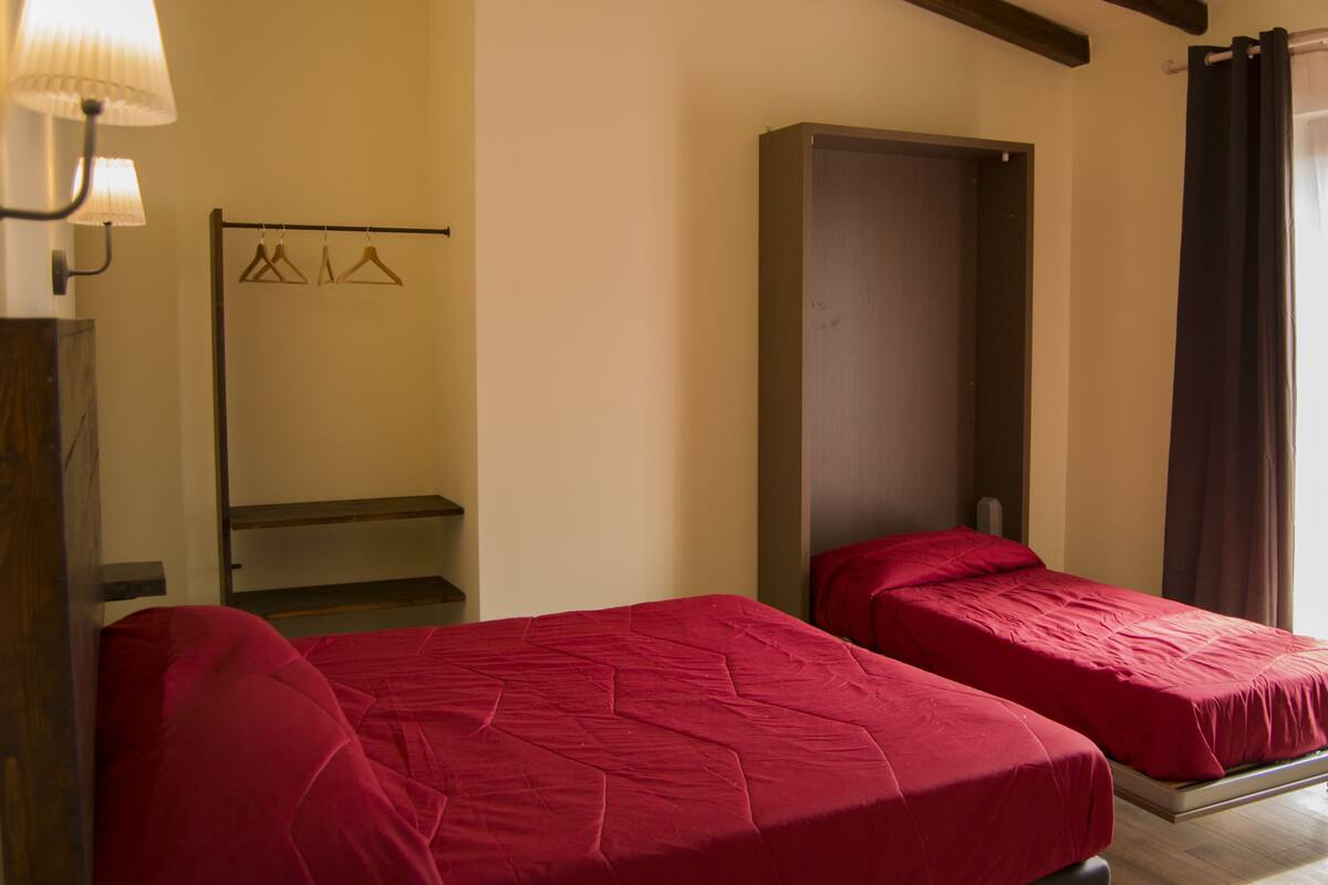 A room with two single beds, a wooden bench, a coat rack with hangers, and a door.