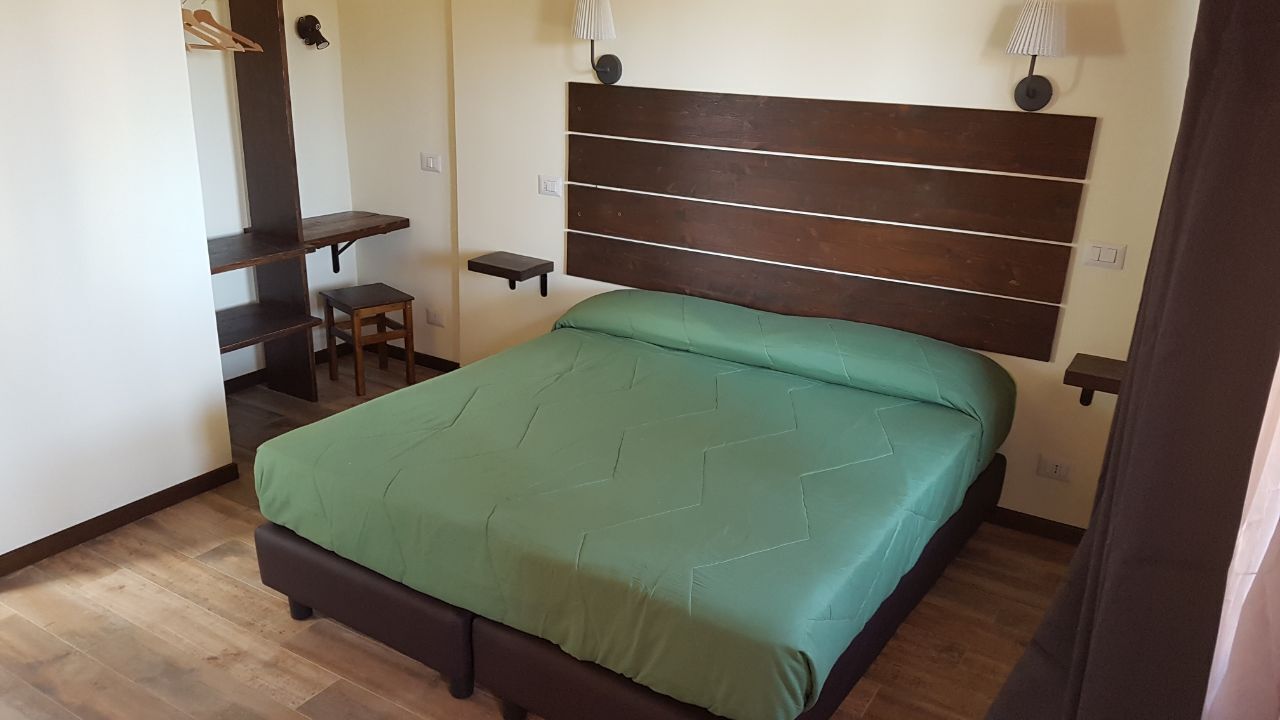 Ein Schlafzimmer mit Bett, Holz-Kopfstück, kleinem Tisch, Stuhl und Regal.