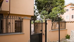 A gated entrance with a metal gate, a stone pathway, and a small garden area with plants and a lamp post. - Sleep and go Hotel (Fiumicino)