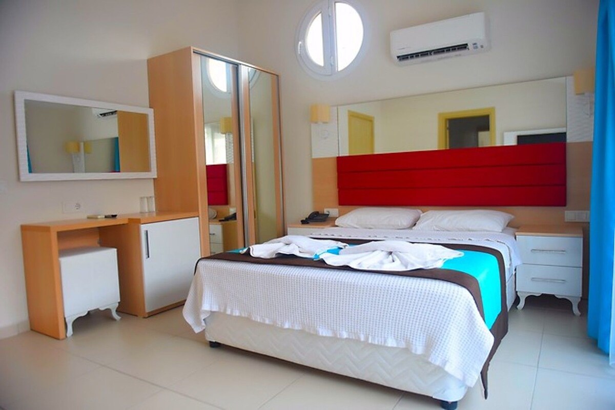 A bedroom with a bed, a desk, a wardrobe, a mirror, and an air conditioning unit.