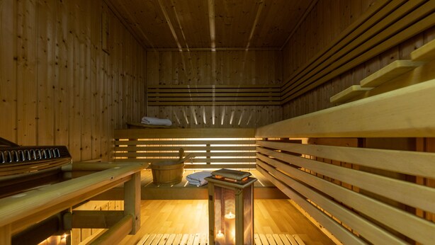 Una sauna con bancos de madera, un banco con una toalla y una vela en el suelo.