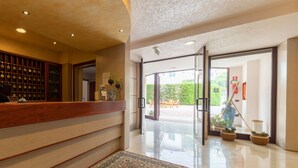Un vestíbulo de hotel con mostrador de recepción, alfombra estampada y puerta de vidrio que da al exterior.