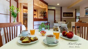 Una mesa de desayuno con diversos alimentos y bebidas, un florero con flores y un cuadro en la pared.
