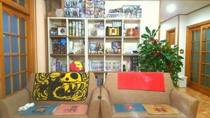 Una sala de estar acogedora con una estantería llena de objetos varios, un sofá con cojines coloridos y una planta en maceta.