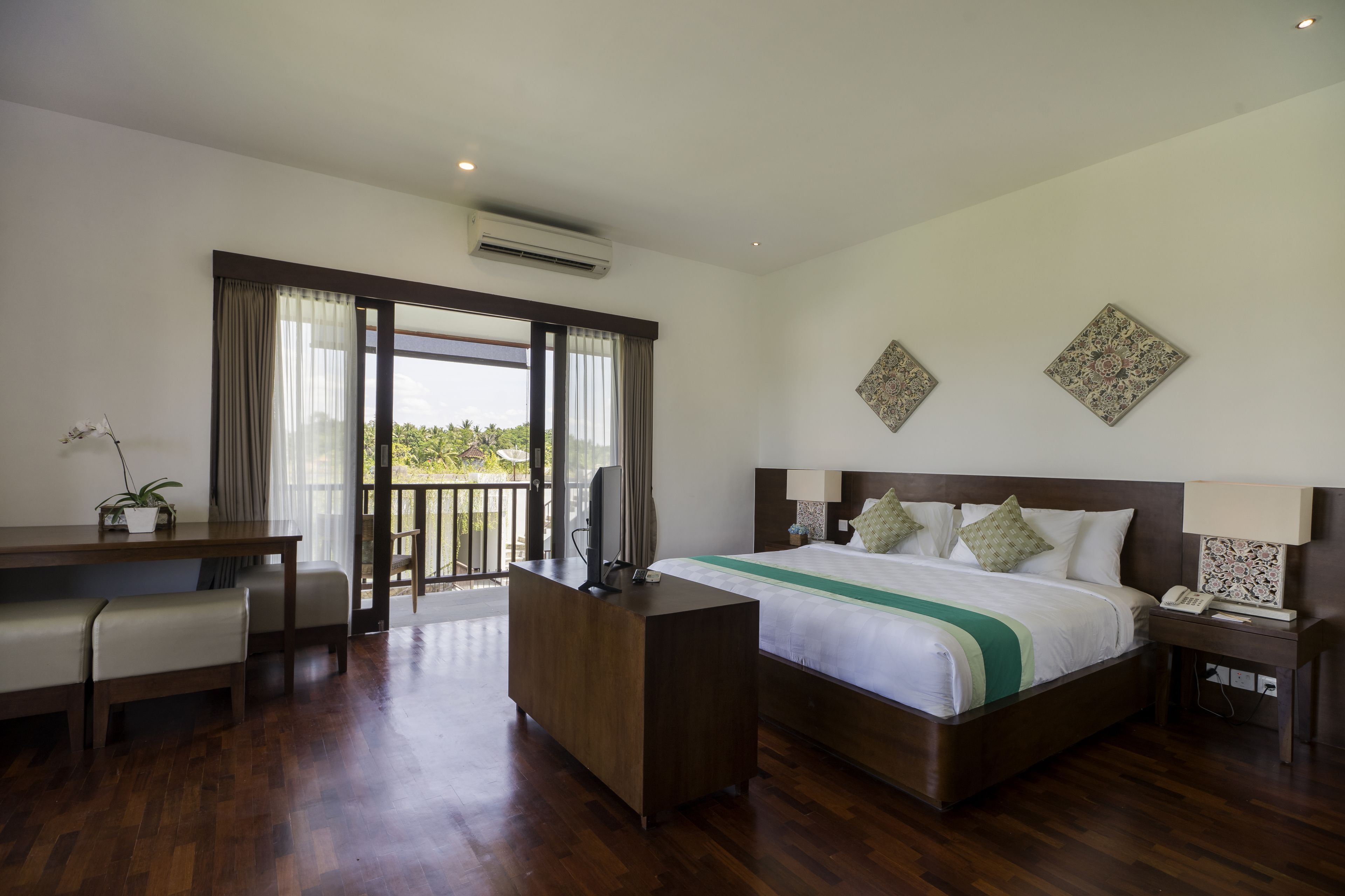 A spacious hotel room with a large bed, a desk, a chair, a TV, and a balcony with a view.