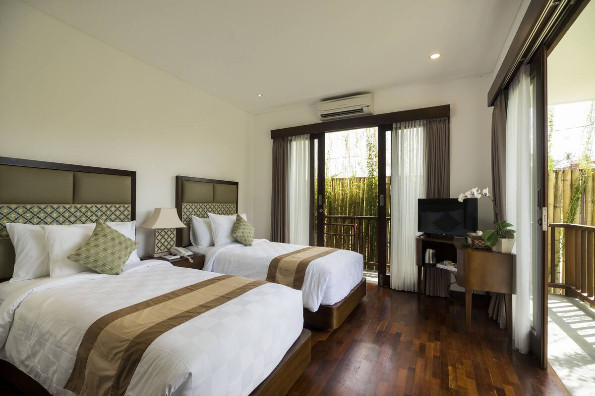 A hotel room with two beds, a TV, a desk, and a balcony with a view.