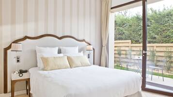 Une chambre d’hôtel avec un grand lit, une table de chevet avec une lampe et une vue sur une terrasse agrémentée de chaises et de plantes.