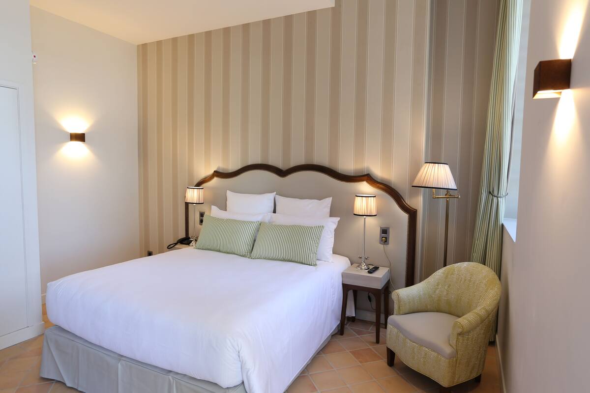Une chambre d’hôtel avec un grand lit, deux lampes de chevet, une chaise et un mur à rayures.