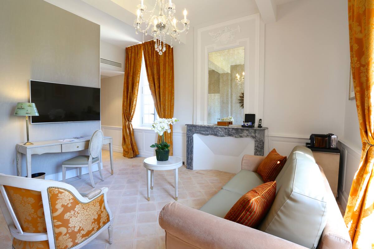 Un salon comprenant un téléviseur, un canapé, des fauteuils, une petite table et une cheminée.