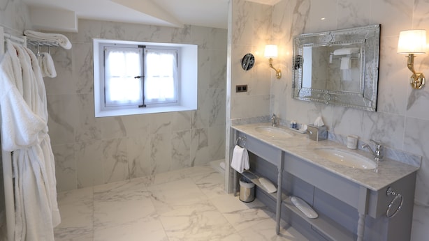 A bathroom with marble walls, a double sink vanity, a large mirror, and a window with a view. - Château de Drudas (Drudas)
